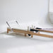 Foldable Pilates reformer with white pads and maple oak frame for space-saving studios