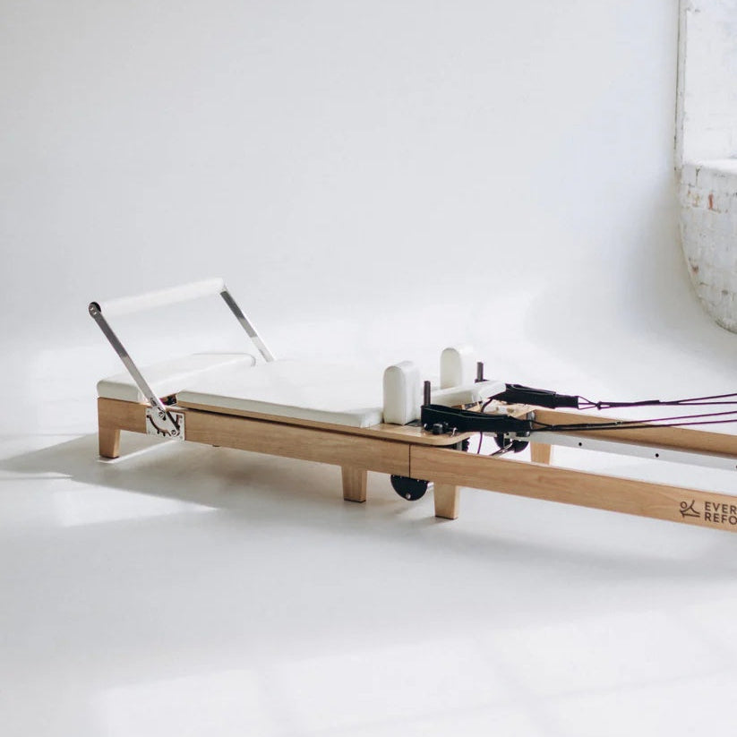Foldable Pilates reformer with white pads and maple oak frame for space-saving studios